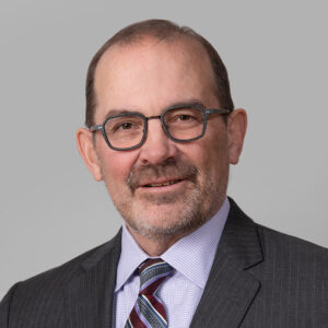 Professional headshot of Bradley Swallow, Shareholder at Shulman Rogers, wearing a charcoal pinstripe suit and striped tie against a neutral gray background